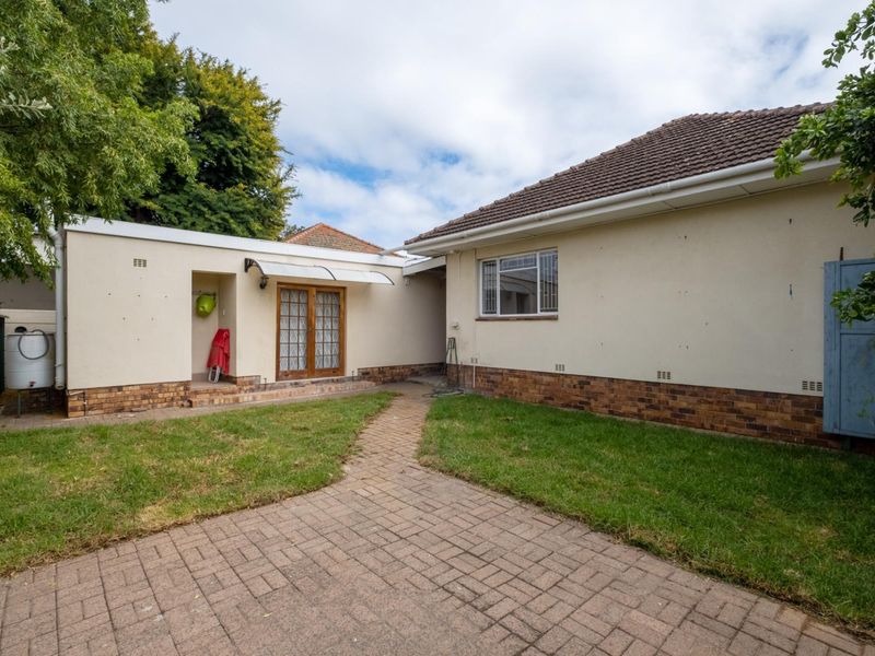 Rear view of the property featuring a paved walkway, lawn area, brick plinth detailing, and access via french doors.