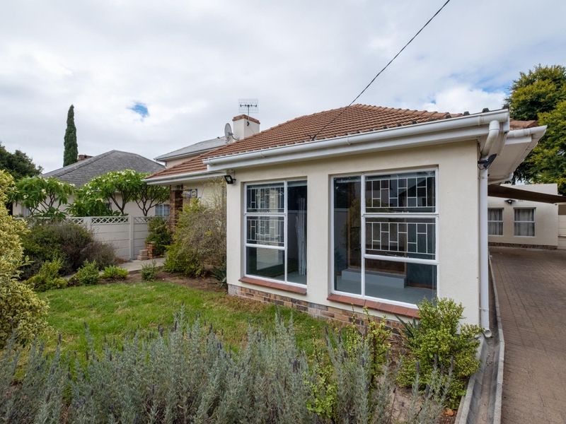 Front view of a residential apartment featuring a tiled roof, paved driveway, and security-fitted windows, set within a landscaped garden area.