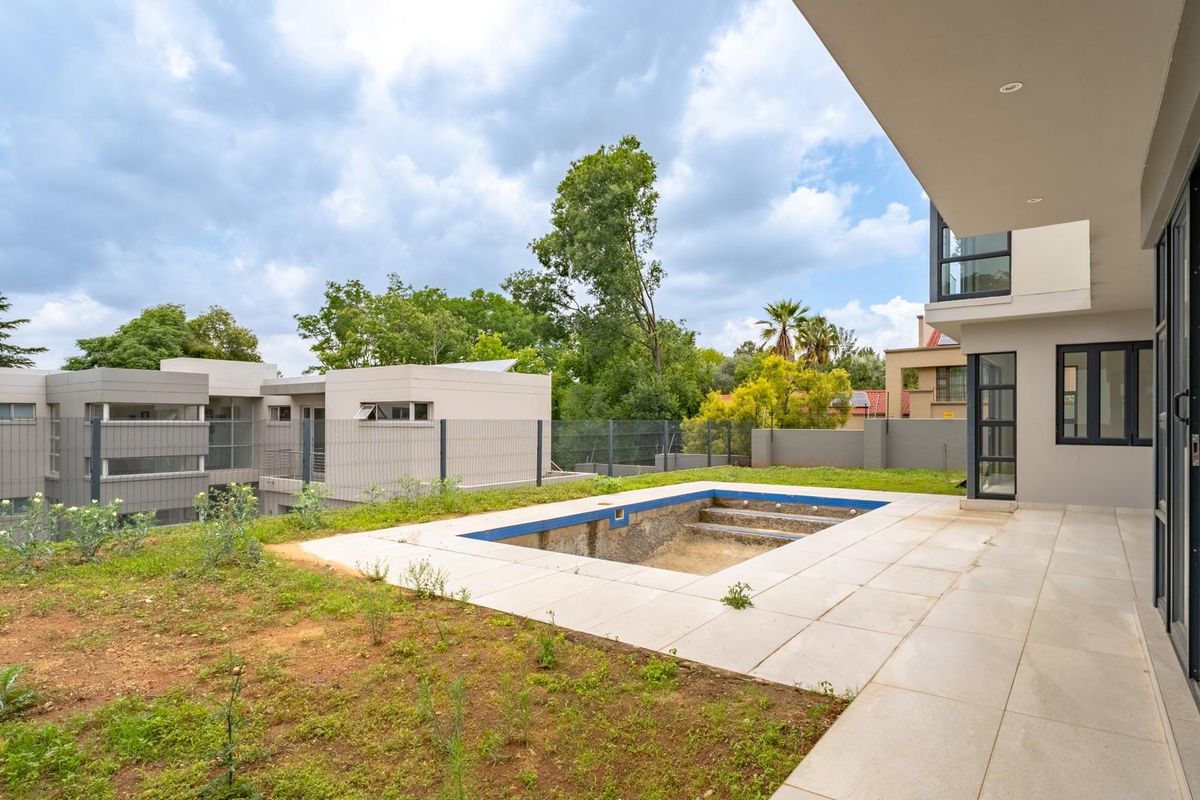 Rear view of the property featuring a covered patio area and an empty, unfinished swimming pool set within a partially landscaped garden.