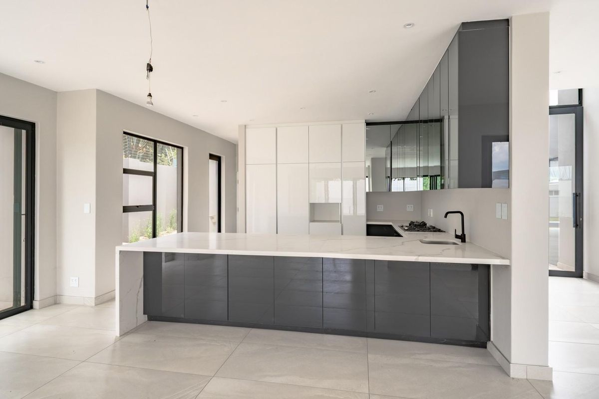 Modern open-plan kitchen featuring high-gloss cabinetry, a large stone-topped island, integrated appliances, and sleek black fixtures in a bright, contemporary space.