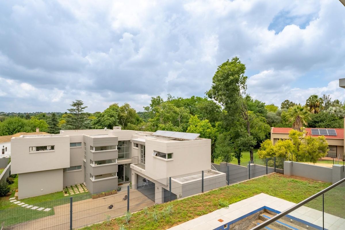 Elevated view of a modern multi-level residence featuring solar panels, a paved driveway, and a landscaped garden area.