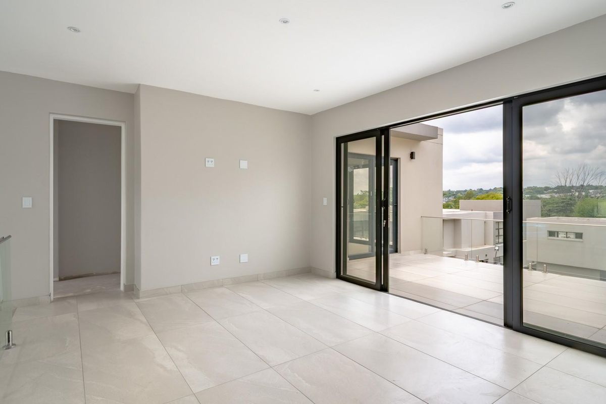 A bright, modern living area featuring large sliding glass doors that open onto a spacious balcony with glass balustrades and neutral tiled flooring.
