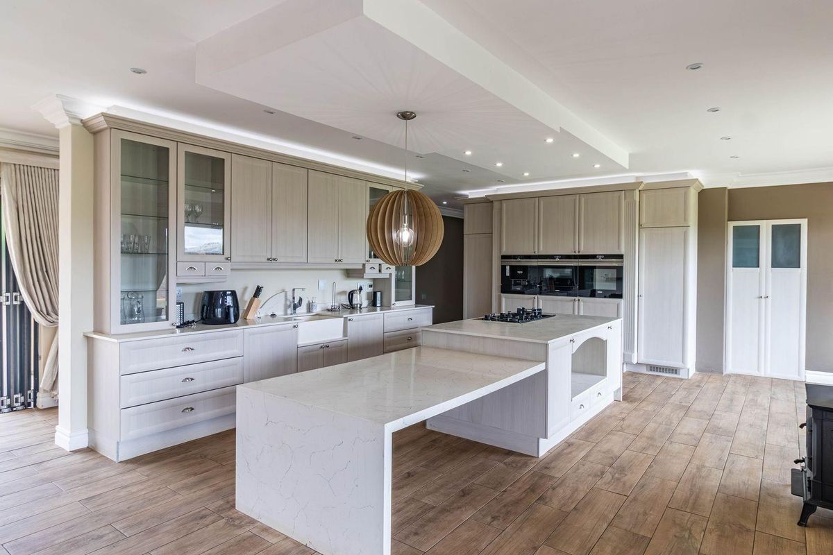 Modern open-plan kitchen featuring light wood cabinetry, stone countertops, a central island with integrated hob, and a wood-burning stove.
