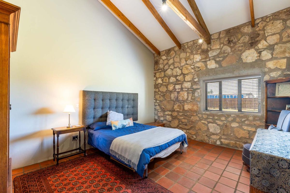 A rustic bedroom featuring exposed timber ceiling beams, a prominent natural stone feature wall, and traditional terracotta floor tiles.