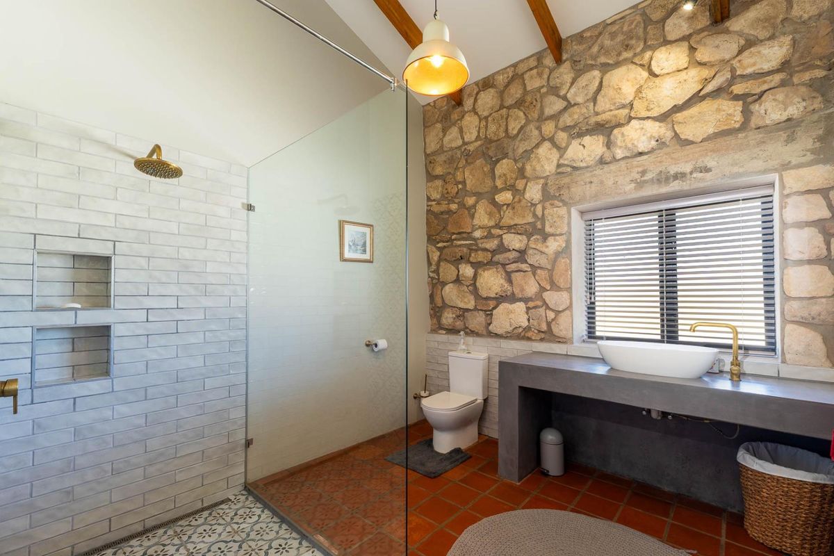 A rustic-style bathroom featuring a stone feature wall, walk-in glass shower with brass fixtures, and a concrete vanity with a vessel sink.