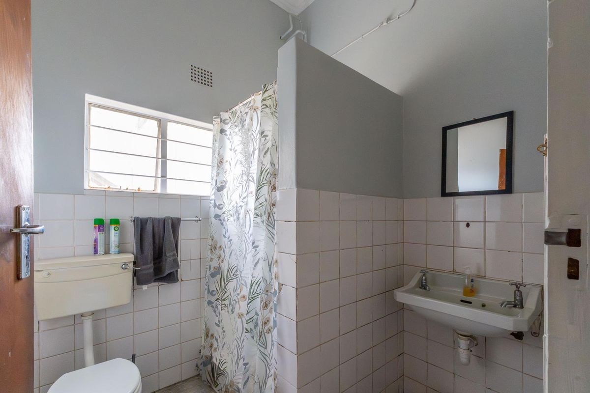 A functional bathroom featuring a wall-mounted basin, toilet, and a shower area with tiled walls and a privacy partition.