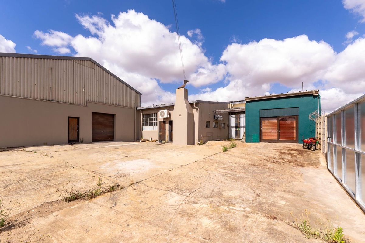 Exterior view of a commercial property featuring a large concrete yard, industrial warehouse structure, and multiple access points.