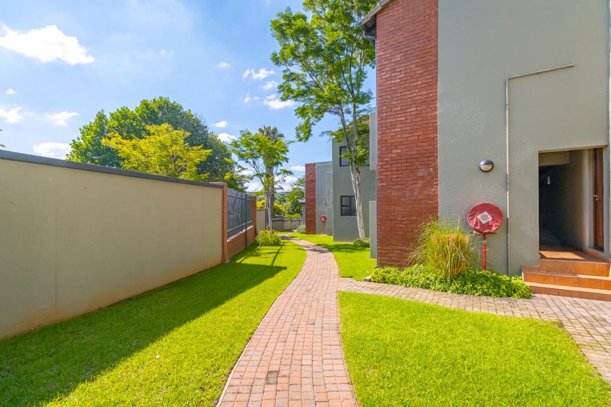 A well-maintained exterior pathway leading through a landscaped garden area between apartment building blocks with brick facade detailing.