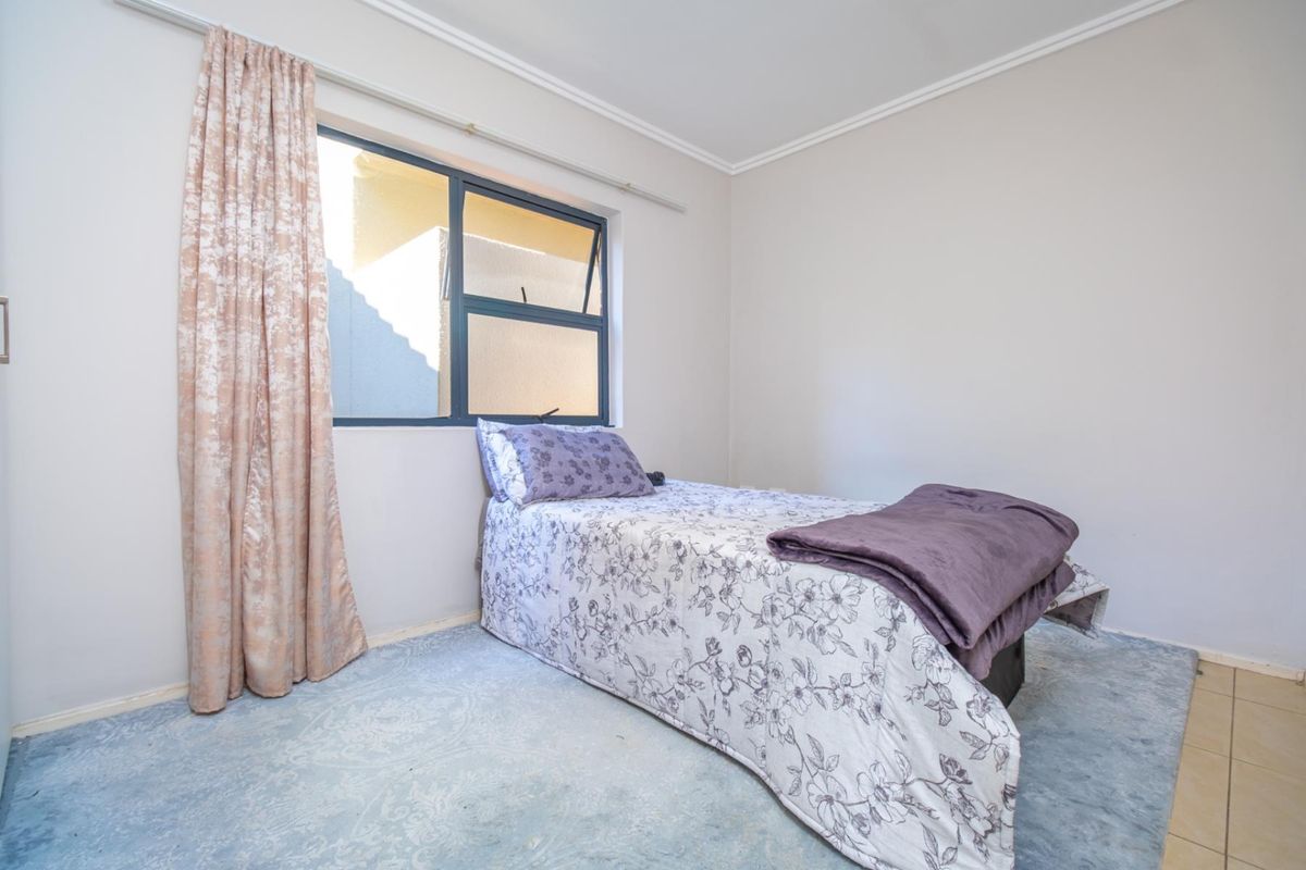 A functional bedroom featuring neutral walls, a window with curtain track, and carpeted flooring.