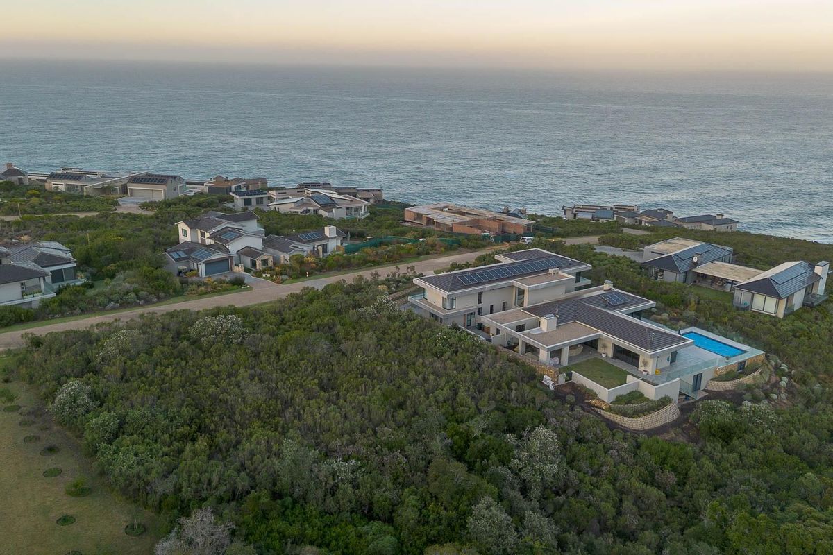 Aerial view of a coastal residential estate featuring modern homes with solar panels, swimming pools, and landscaped surroundings overlooking the ocean.