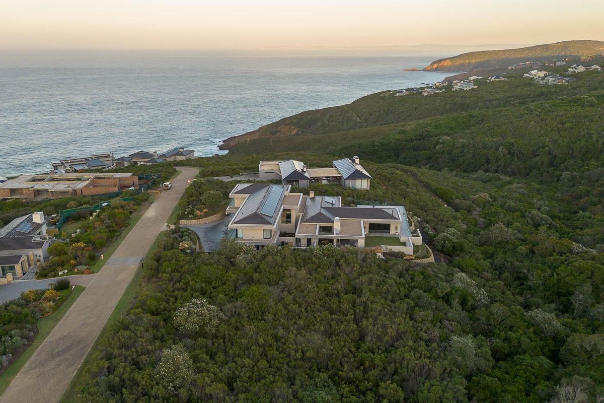 Aerial view of a luxury coastal residential property situated on a hillside, showcasing the building layout, surrounding vegetation, and proximity to the ocean.