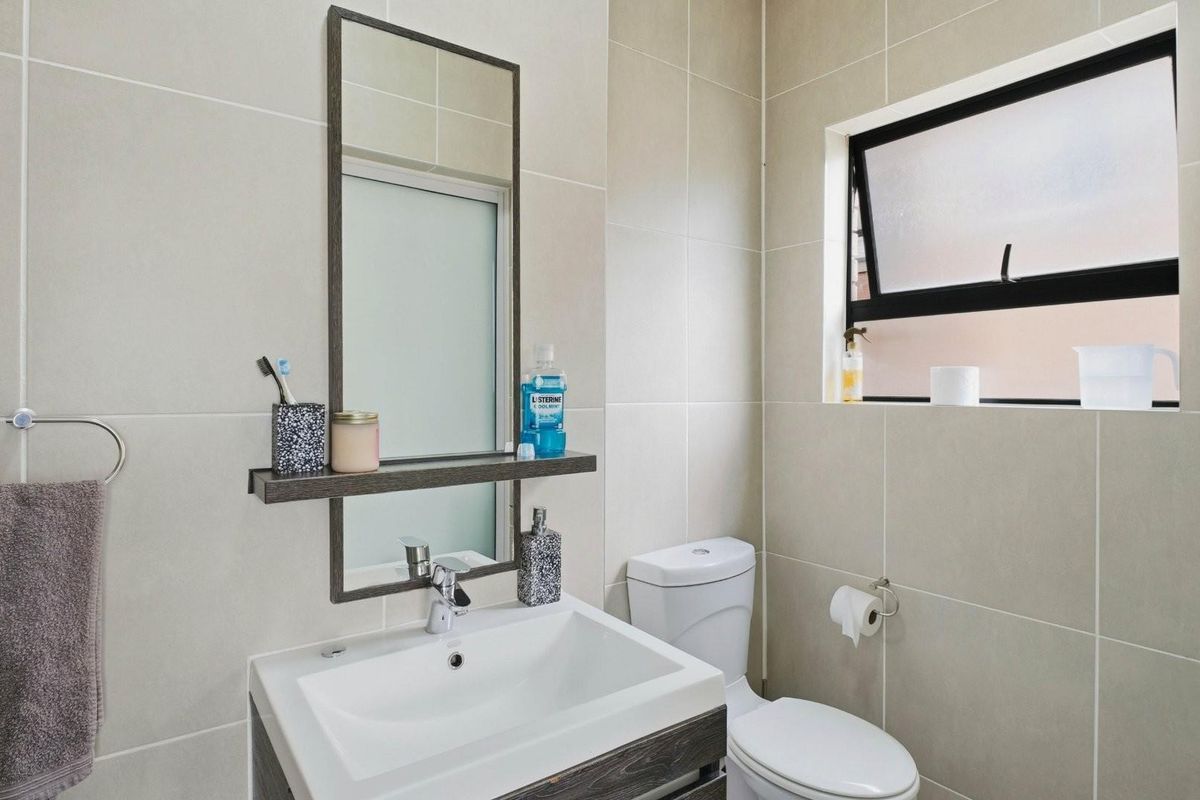 A modern bathroom featuring neutral wall tiles, a contemporary vanity with integrated basin, a wall-mounted mirror, and a functional top-hung window.