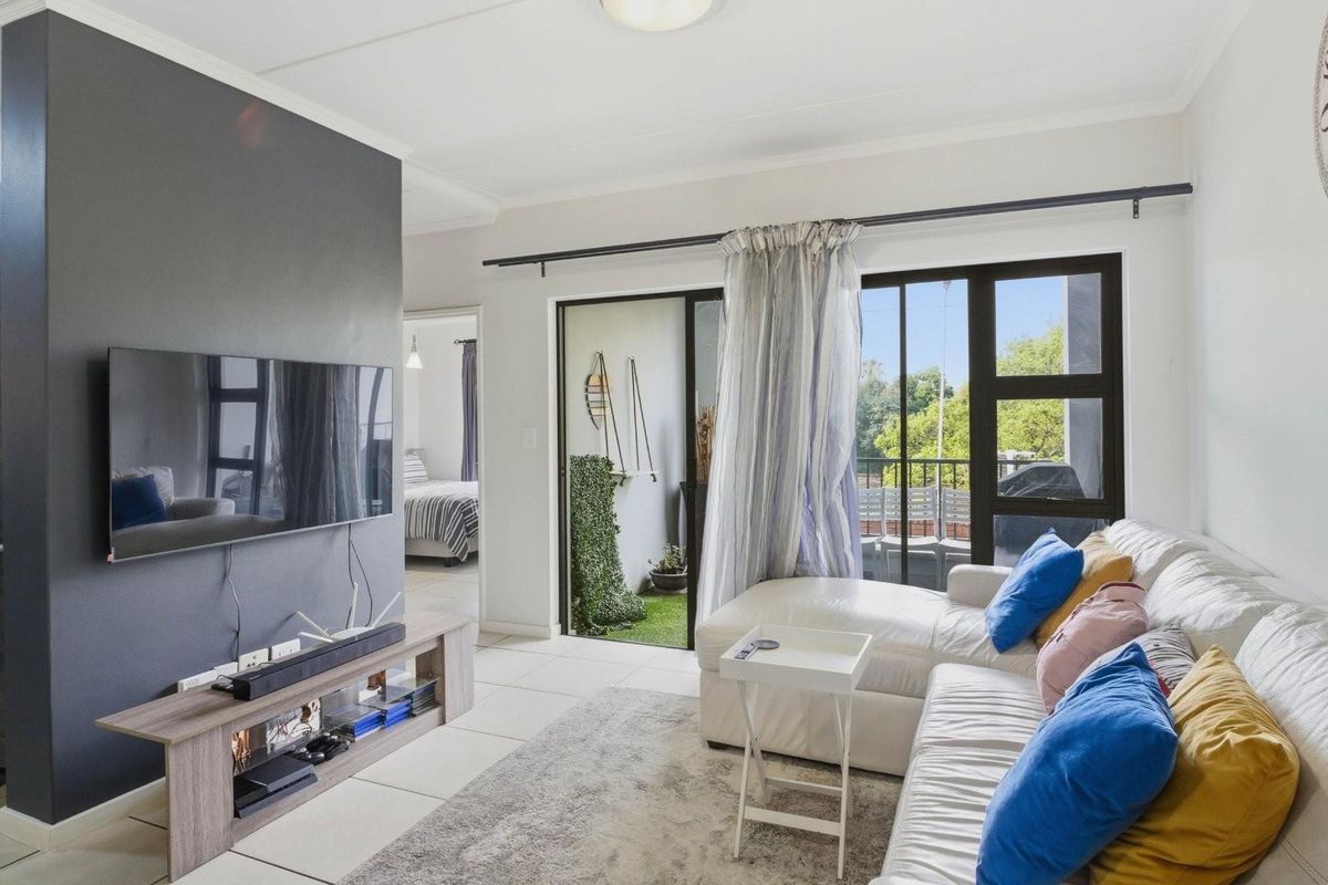 A bright living room featuring tiled flooring, a feature wall, and sliding glass doors that open onto a private balcony.