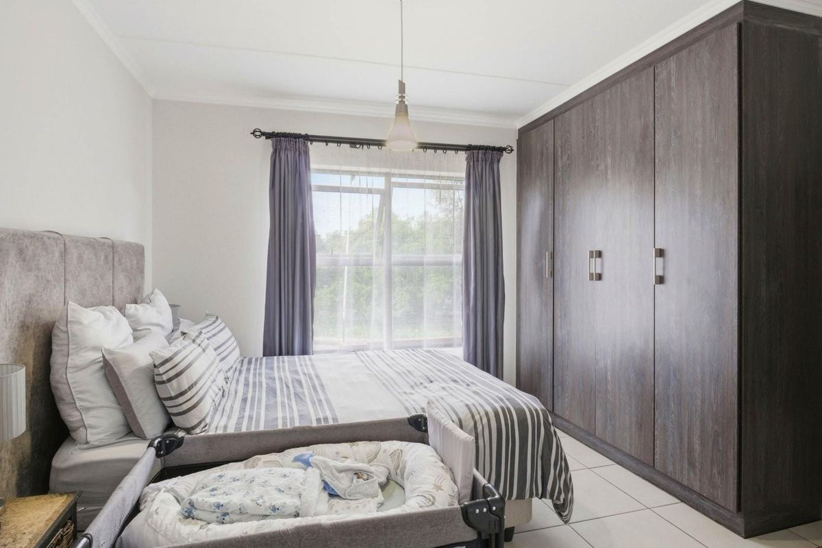 A well-maintained bedroom featuring large built-in wooden wardrobes, tiled flooring, and a window providing natural light.