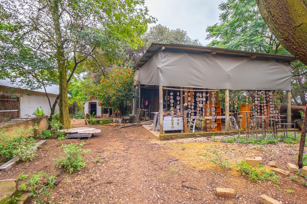 A rustic outdoor workshop or utility structure featuring a corrugated metal roof and open-sided design, situated within a natural garden setting.