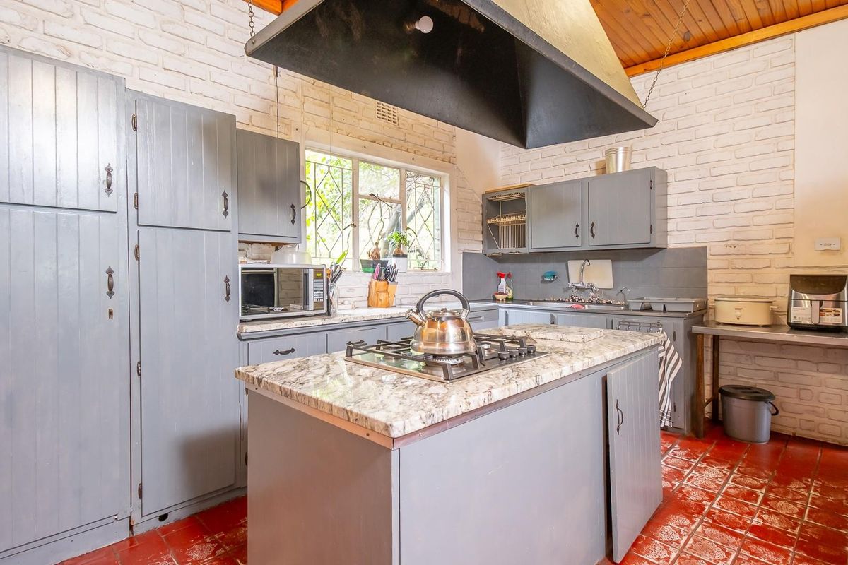 Rustic kitchen featuring a central island with a built-in gas hob, overhead extractor hood, painted cabinetry, and exposed brick walls.