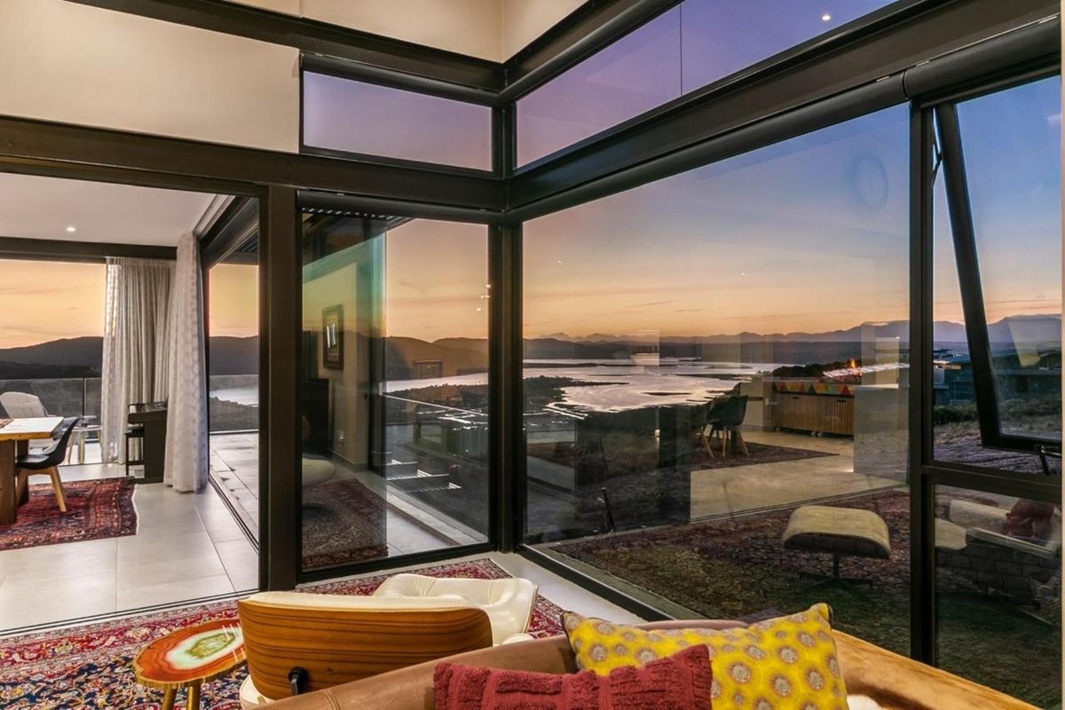 Modern living area featuring expansive floor-to-ceiling corner windows that frame panoramic sunset views over the water and surrounding landscape.