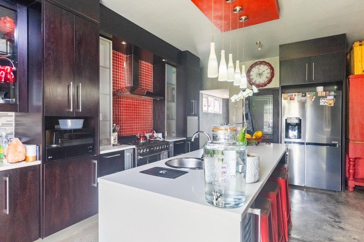 Modern kitchen featuring dark cabinetry, a central island with a built-in sink, red tiled backsplash, and integrated stainless steel appliances.