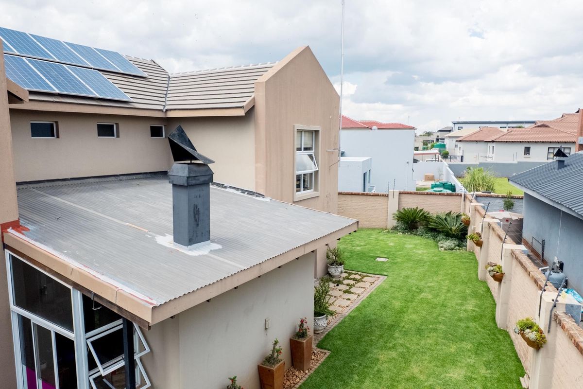Elevated view of the rear garden featuring a lawn, perimeter boundary walls, and a corrugated metal roof section with a chimney and solar panels.