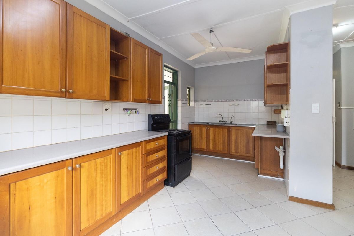 Functional kitchen featuring wooden cabinetry, tiled backsplash, double sink, and a freestanding stove, offering a practical layout with neutral wall finishes.