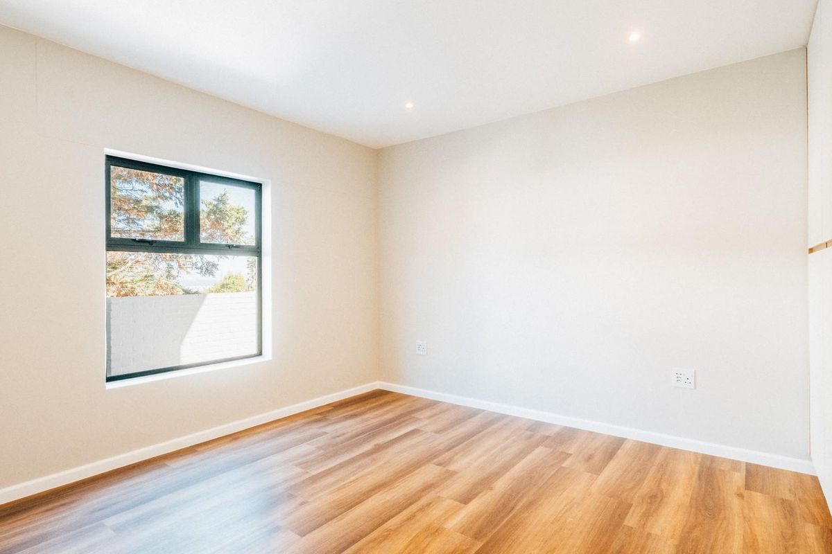 A bright, modern bedroom featuring neutral walls, wood-look flooring, recessed lighting, and built-in cabinetry.