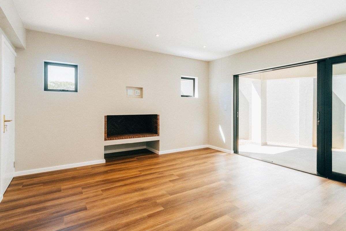 A bright, modern living room featuring wood-look flooring, a built-in fireplace, recessed lighting, and large sliding glass doors opening to an outdoor patio area.