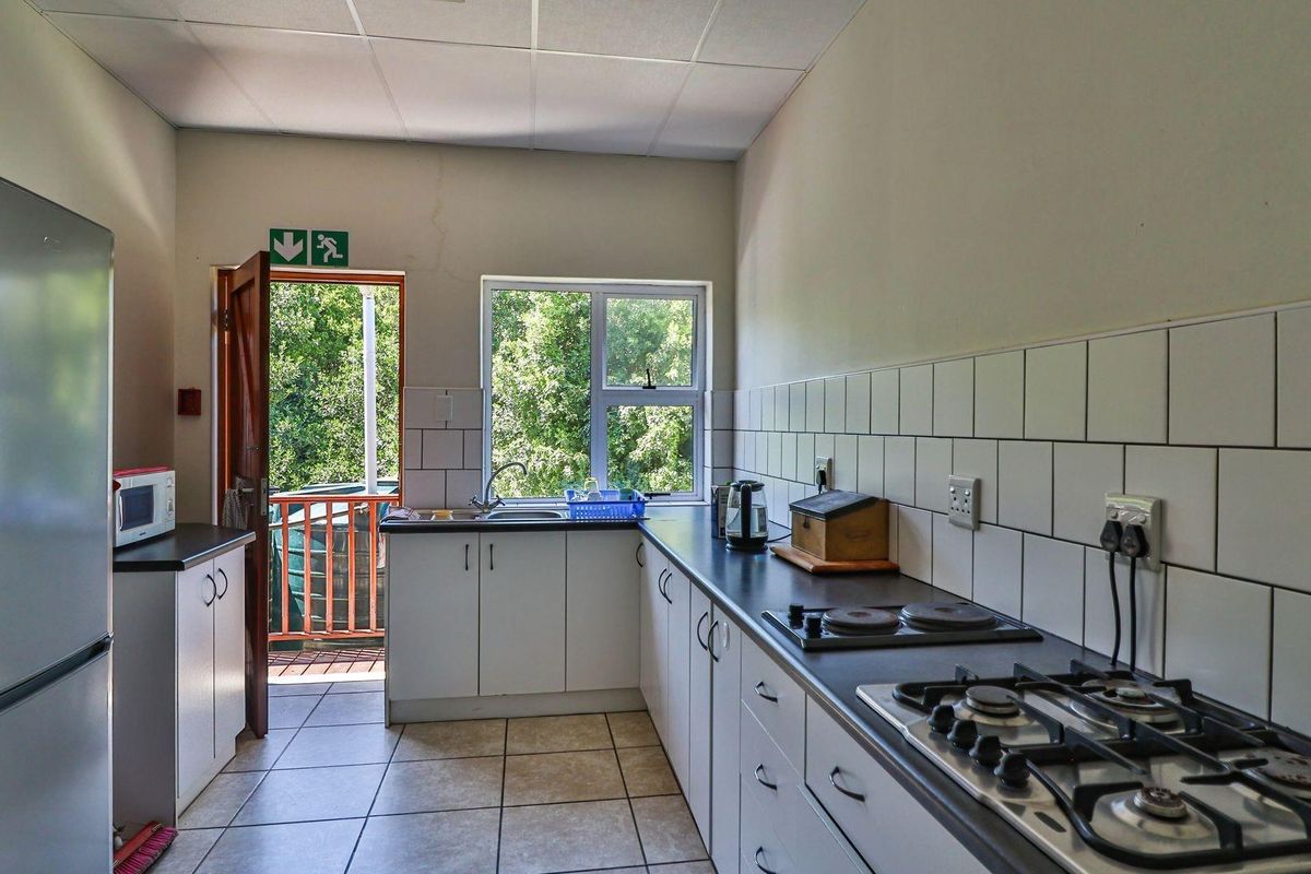 A functional kitchen featuring white cabinetry, tiled splashbacks, a gas hob, and direct access to an outdoor balcony area.