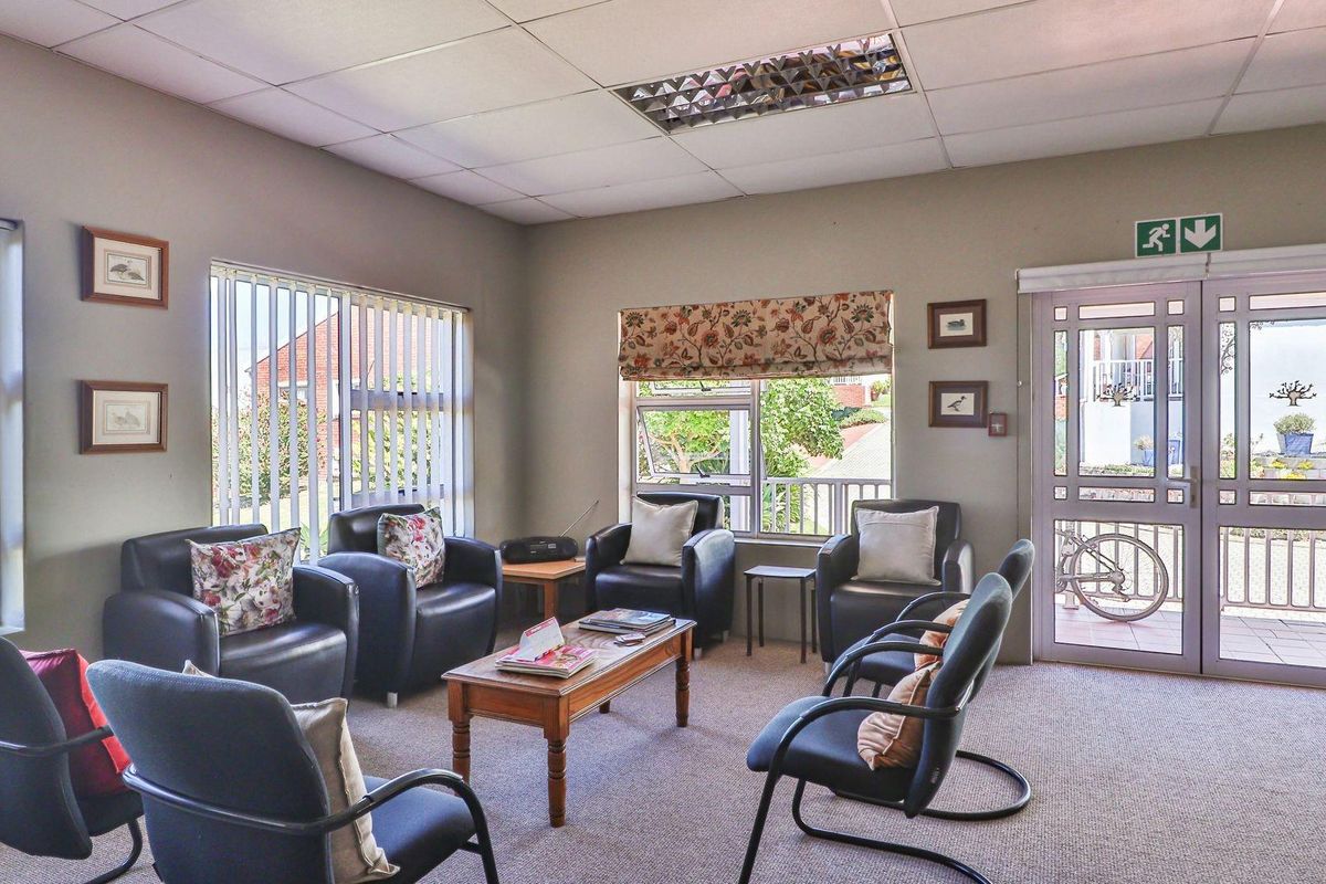 A functional living area featuring neutral carpeting, a suspended ceiling with recessed lighting, and large windows providing natural light and exterior views.