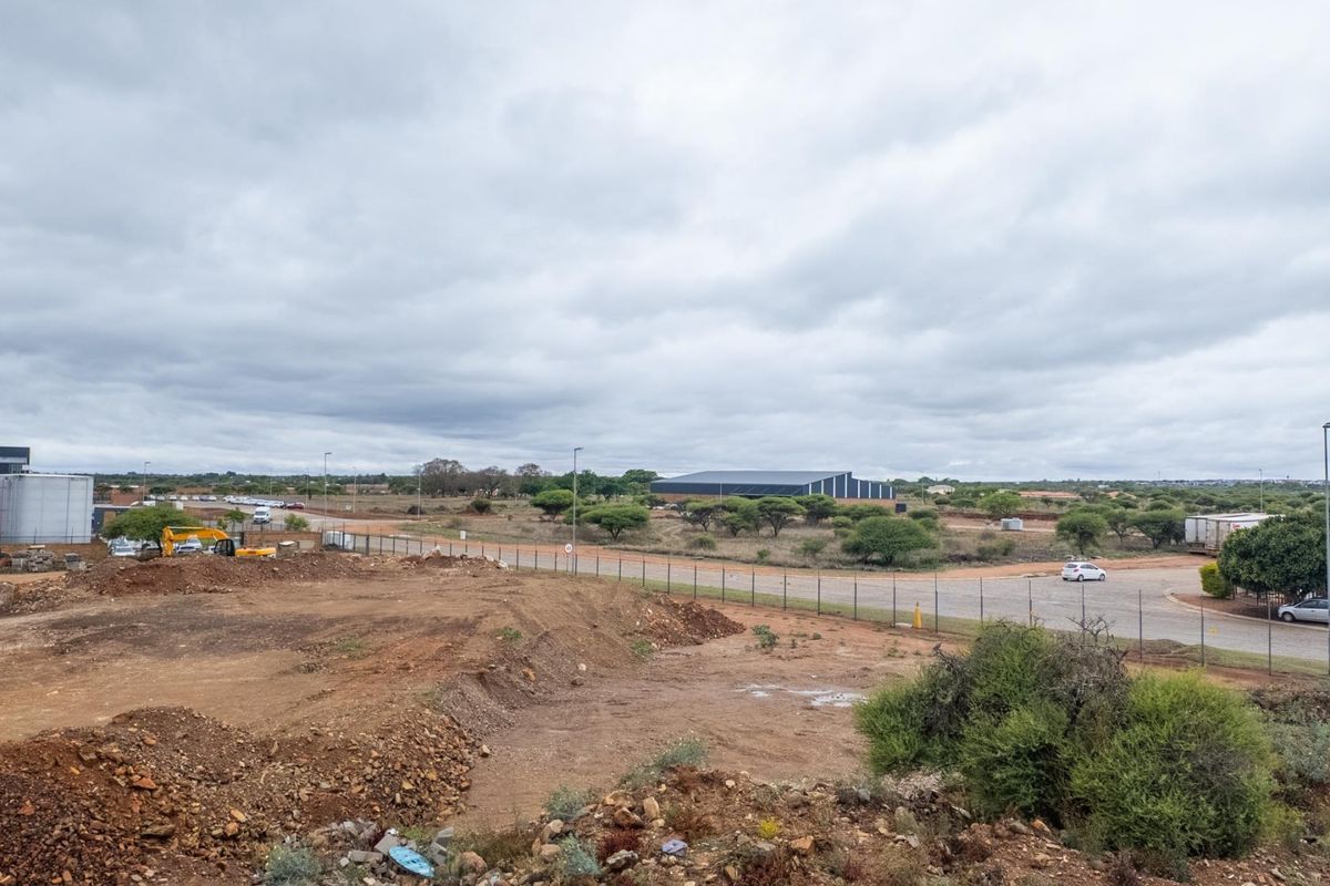 An elevated view of a vacant residential plot featuring natural terrain, surrounding vegetation, and nearby infrastructure under an overcast sky.