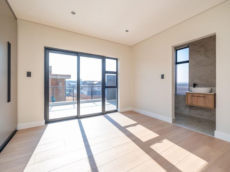 Modern bedroom featuring light wood-look flooring, built-in cabinetry, and an en-suite bathroom with a floating vanity and sliding doors leading to a balcony.