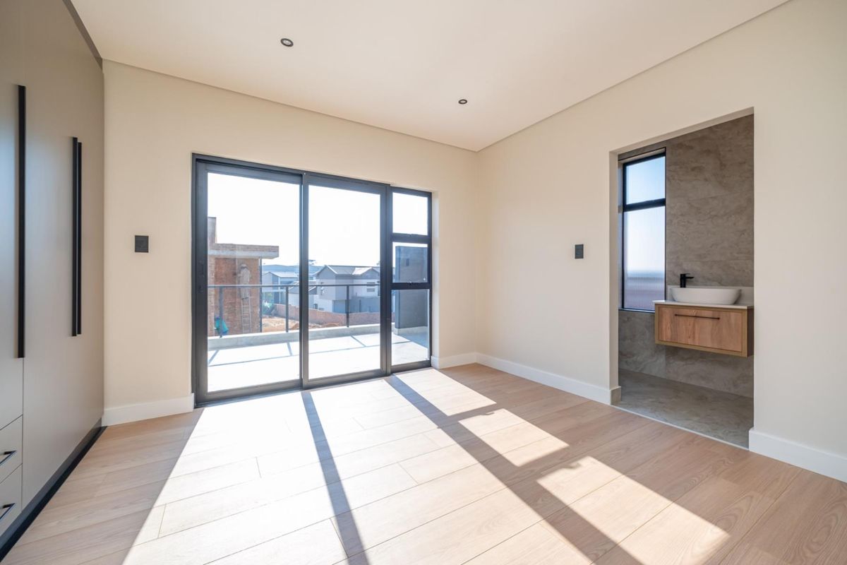 Modern bedroom featuring light wood-look flooring, built-in cabinetry, and an en-suite bathroom with a floating vanity and sliding doors leading to a balcony.