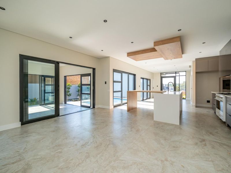 Spacious open-plan living and kitchen area featuring modern cabinetry, a central island, and large sliding glass doors opening to the outdoor patio and pool.