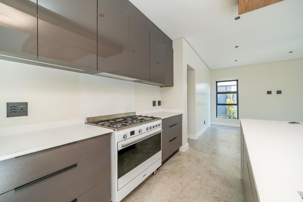 Modern kitchen featuring sleek grey cabinetry, stone countertops, a gas stove, and tiled flooring in a bright, open-plan layout.