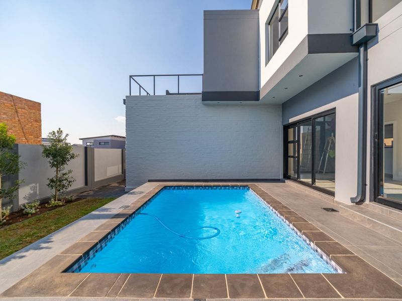 Modern rear exterior featuring a rectangular swimming pool with tiled surround, adjacent to a contemporary two-story home with sliding glass doors.