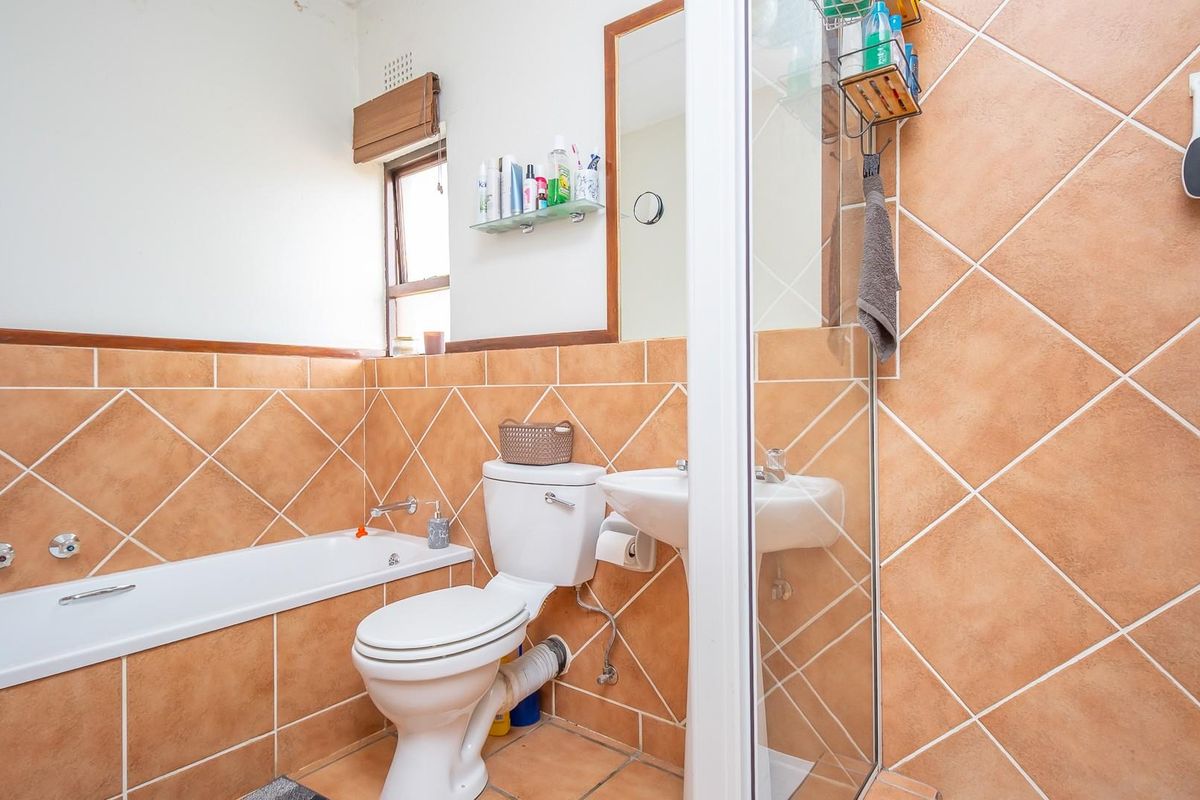 A functional bathroom featuring a bathtub, pedestal sink, and a glass-enclosed shower with terracotta-style wall tiles.