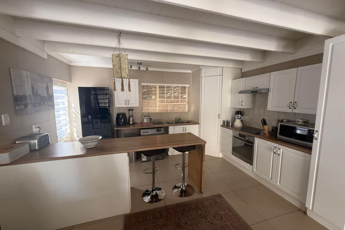 A functional kitchen featuring white cabinetry, a wooden breakfast bar, tiled flooring, and exposed white timber ceiling beams.