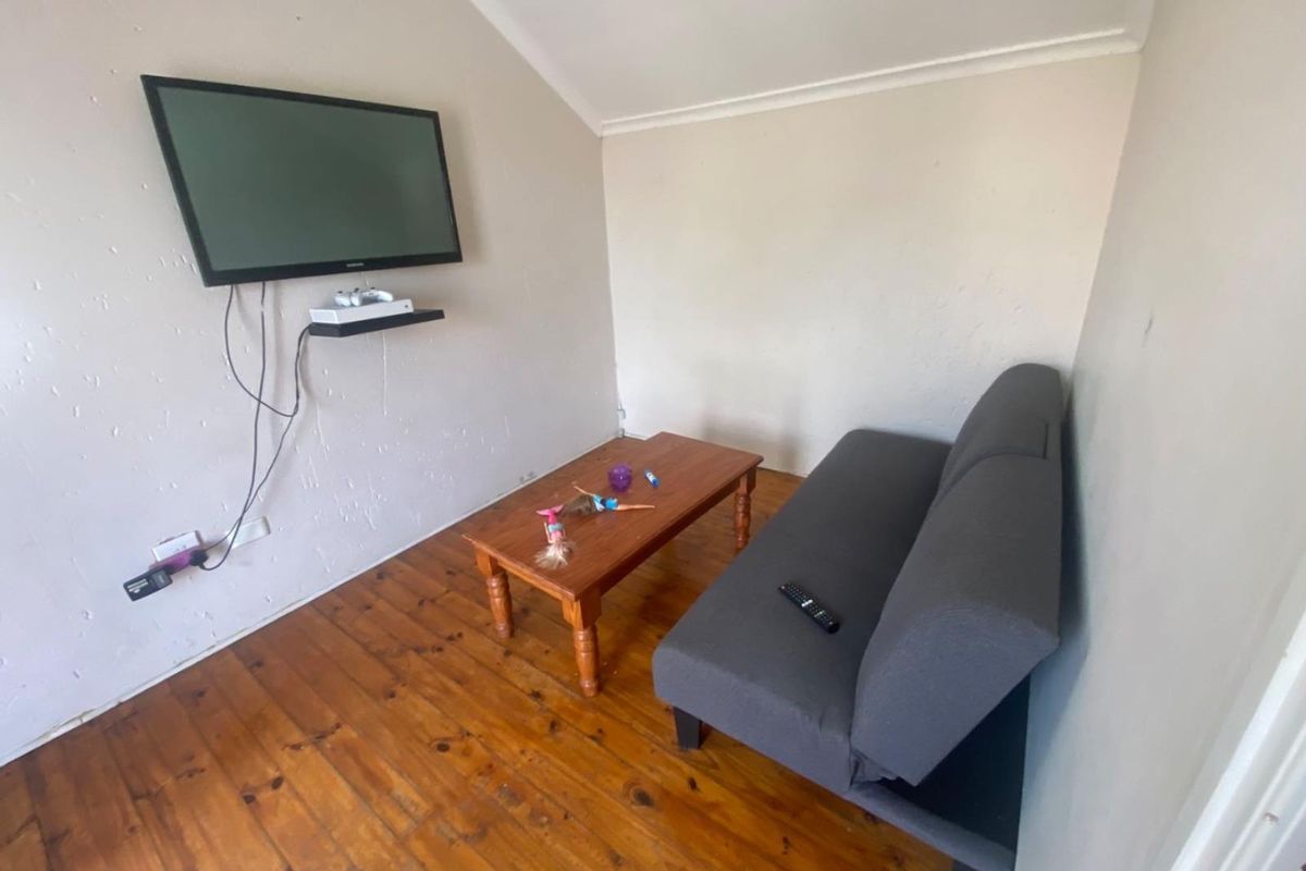 A small living area featuring timber flooring, sloped ceiling, and wall-mounted television setup.
