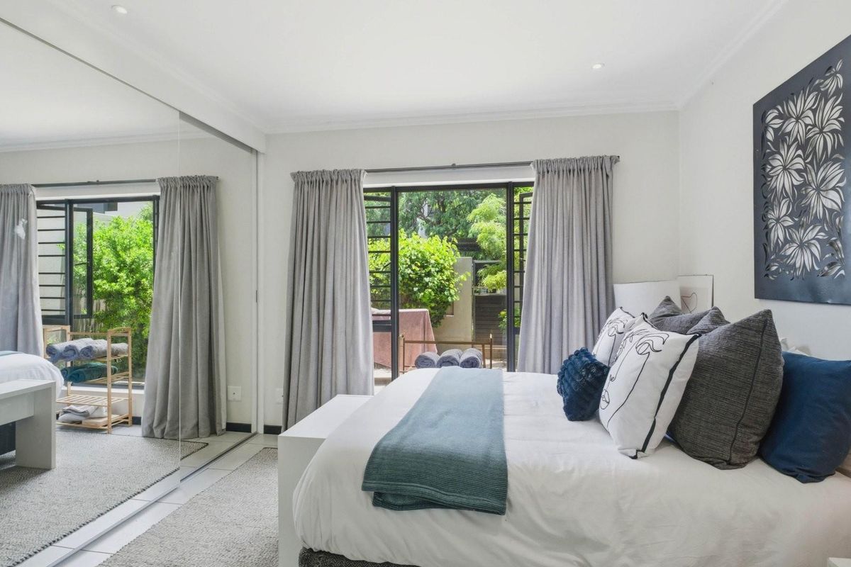 Bright bedroom featuring large mirrored built-in cupboards and direct access to a private outdoor patio area through sliding glass doors.
