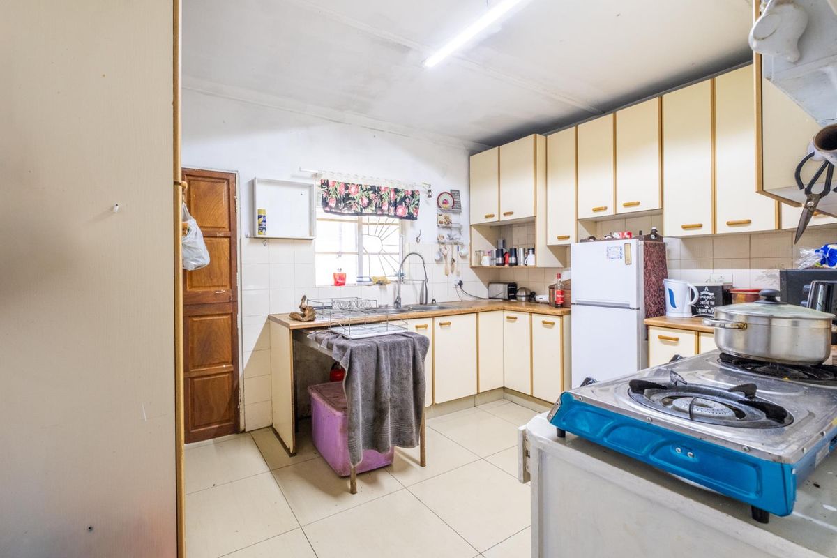 A functional kitchen featuring laminate cabinetry, tiled flooring, and a stainless steel sink, offering a practical layout with potential for modernization.