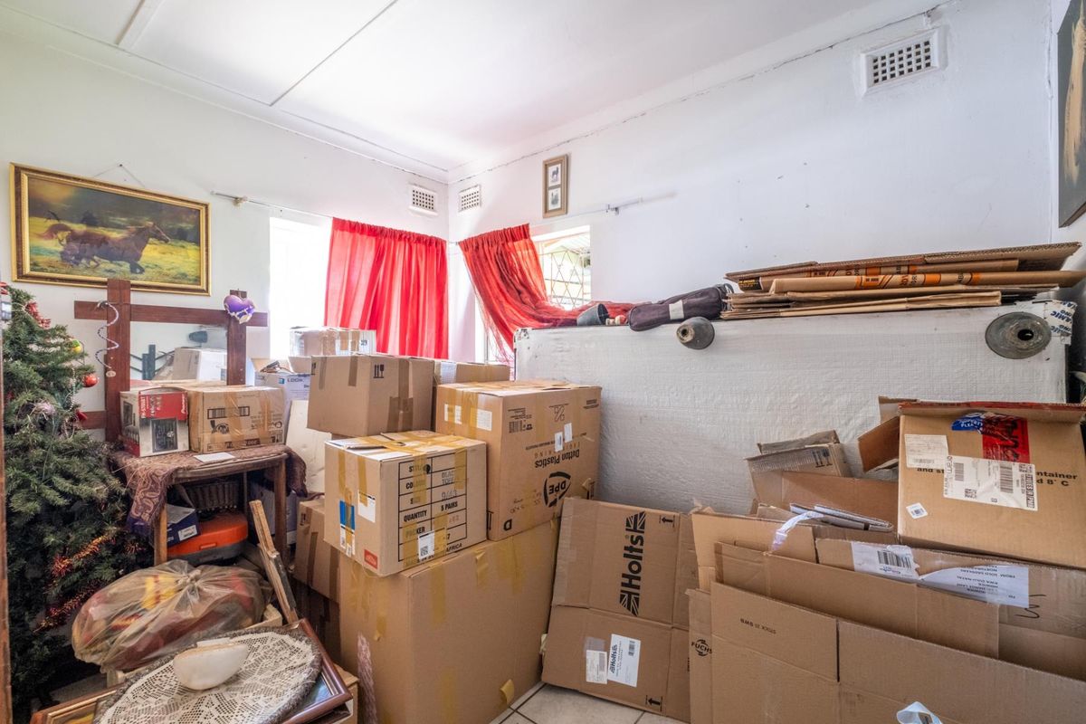 A cluttered interior space featuring tiled flooring, ceiling vents, and standard window treatments, currently used for storage.