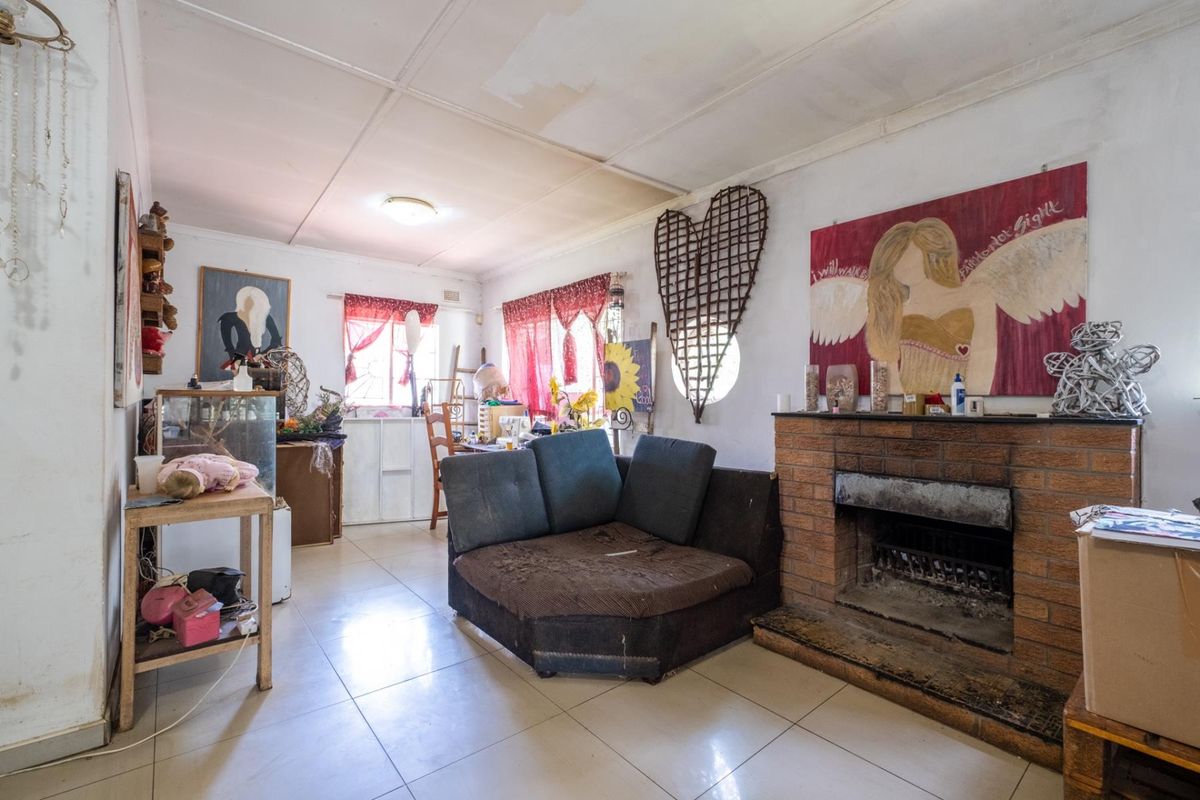 A living room featuring a brick fireplace, tiled flooring, and multiple windows, offering a functional space in need of cosmetic updates.