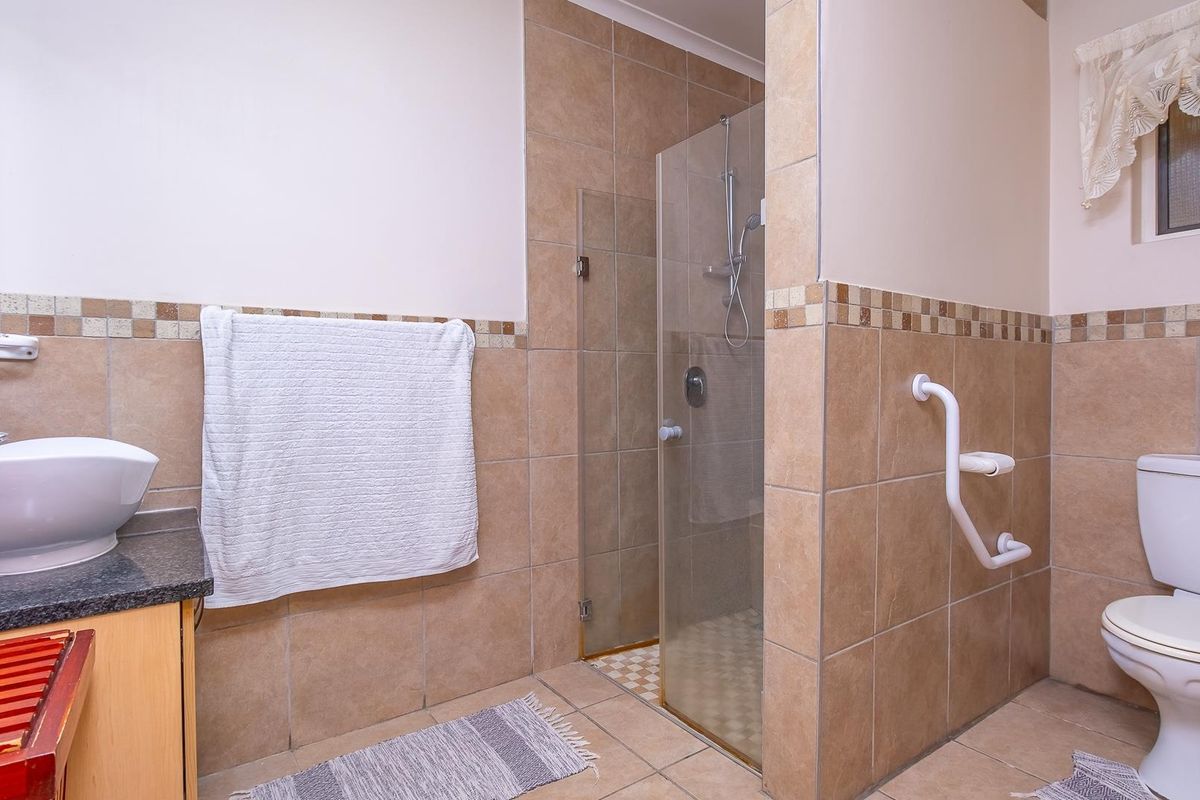 A functional bathroom featuring a vessel sink on a granite vanity, a glass-enclosed shower, and a toilet with an installed grab rail.