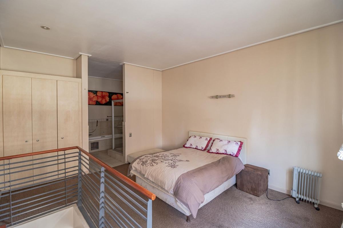 A bedroom featuring built-in cupboards and an en-suite bathroom, overlooking a staircase with a metal balustrade.