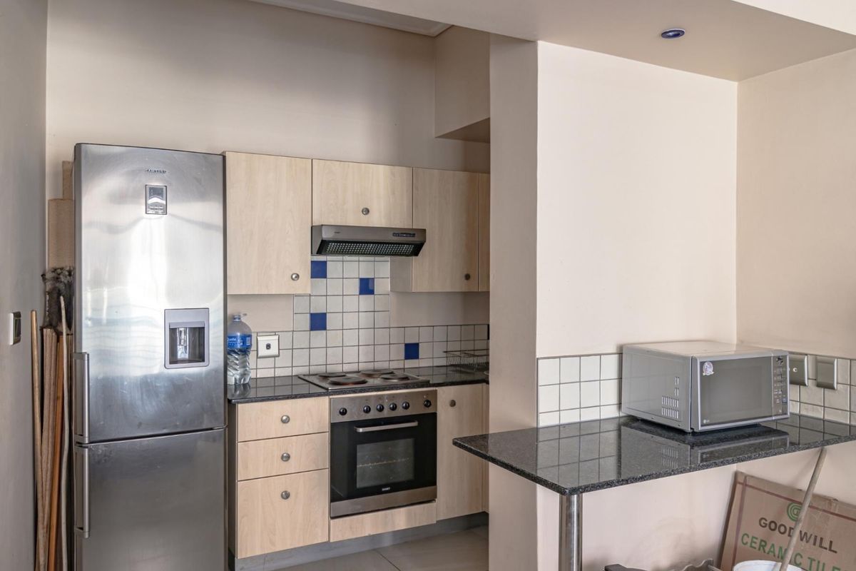 Compact kitchen featuring light wood cabinetry, granite countertops, built-in oven, electric hob, and an integrated extractor fan.