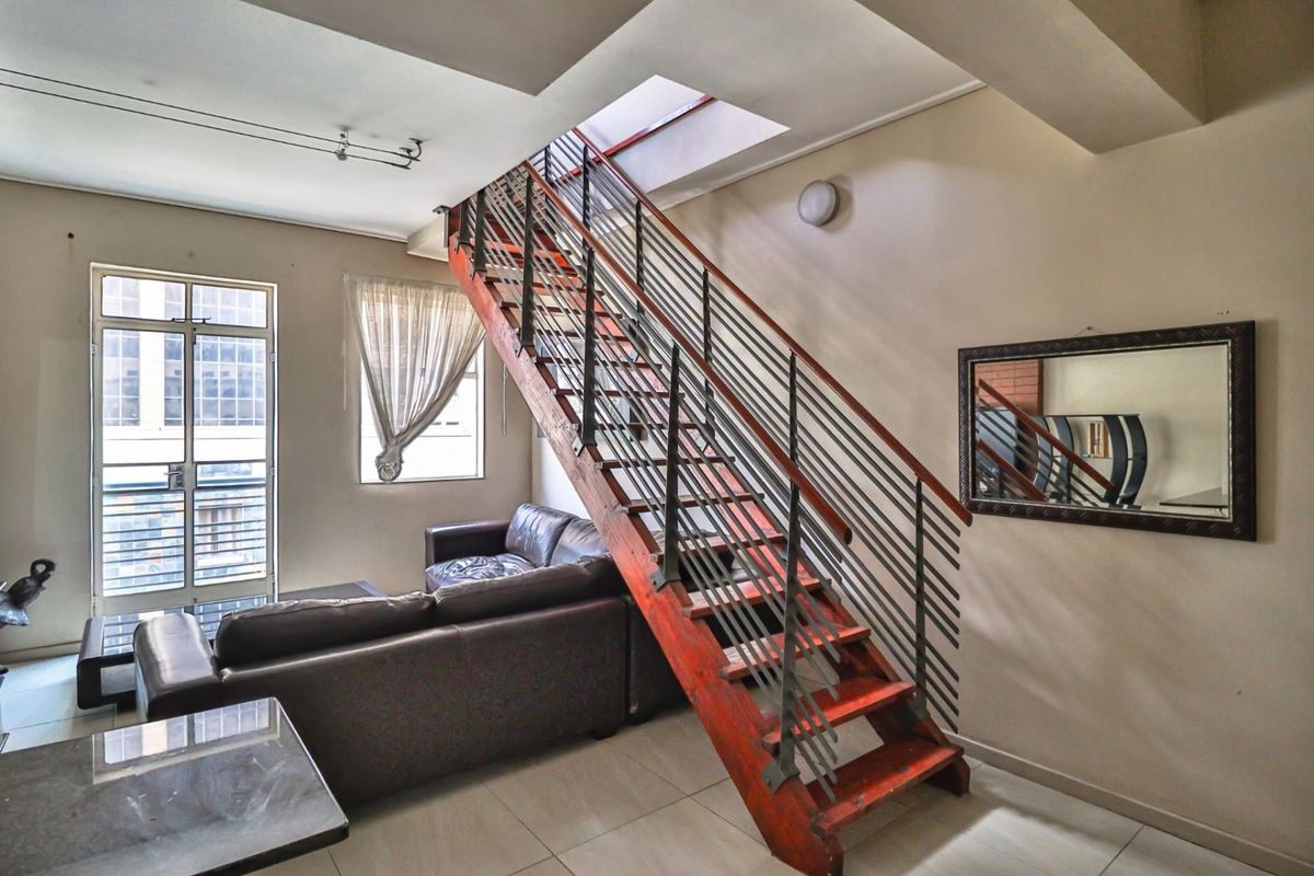 A living area featuring a prominent wooden staircase with metal railings, tiled flooring, and access to a balcony through a glass door.