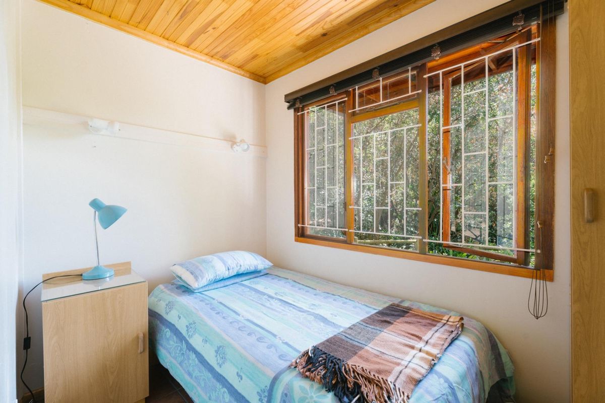 A bedroom featuring a timber-paneled ceiling, wooden window frames with security bars, and natural light.