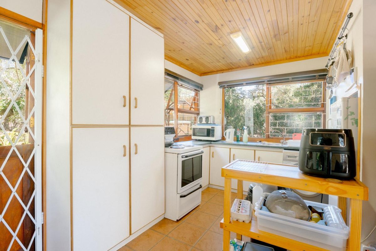 A functional kitchen featuring white cabinetry, a freestanding stove, and large windows with security bars, finished with a timber-paneled ceiling and tiled floors.