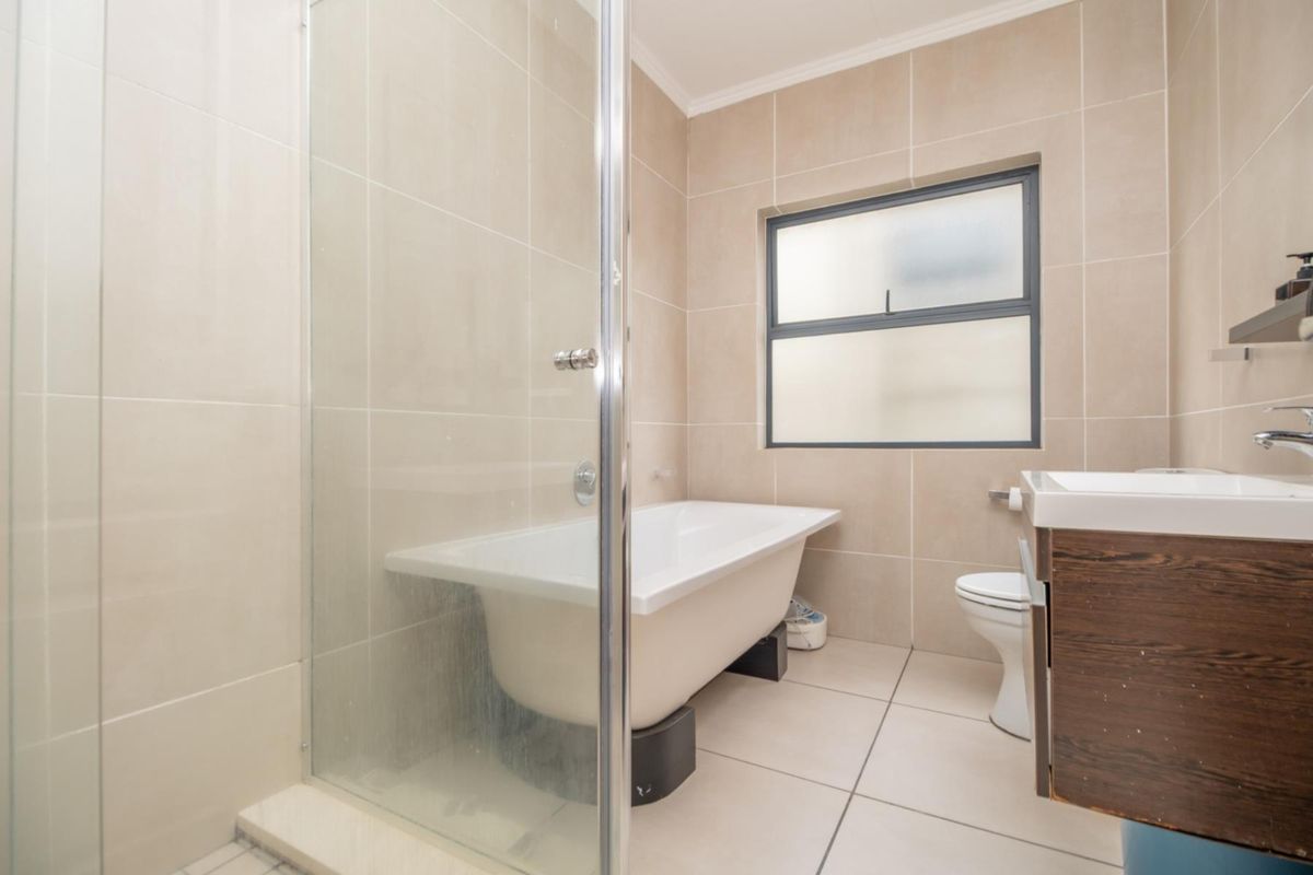 Modern bathroom featuring a freestanding bathtub, glass-enclosed shower, wall-mounted vanity, and neutral floor-to-ceiling tiling.