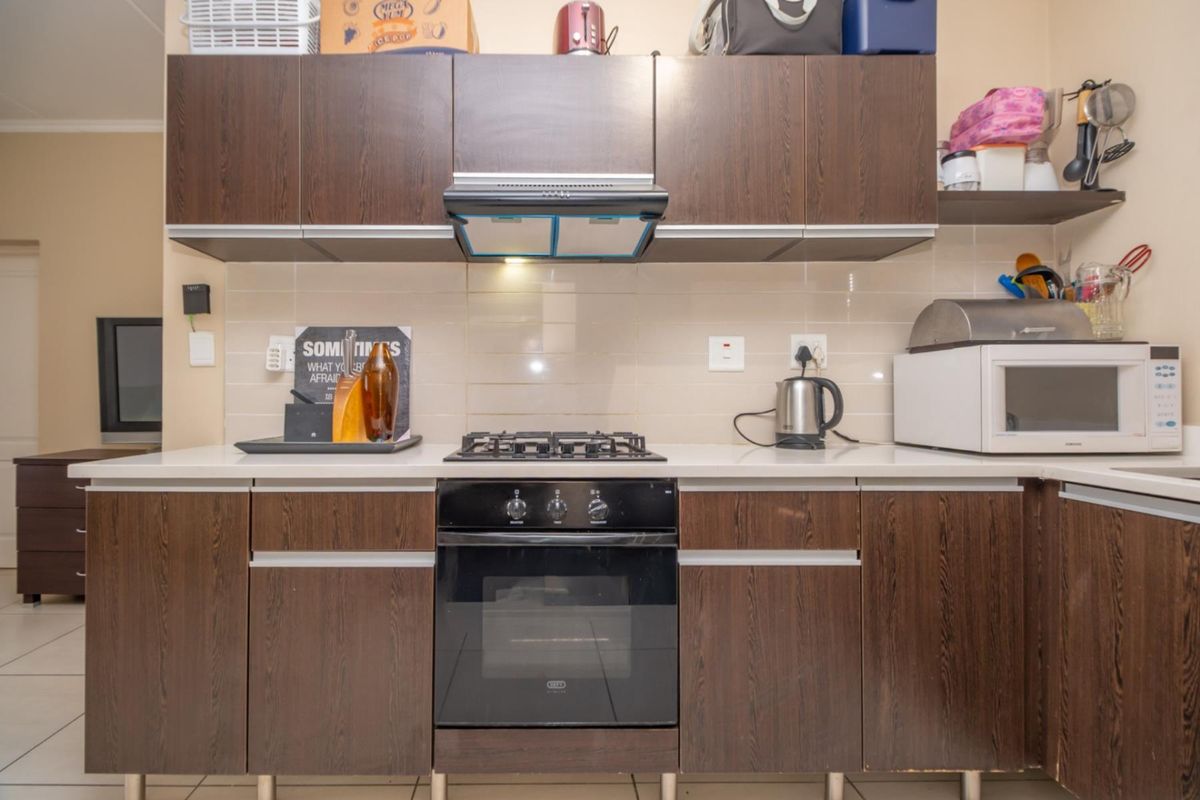 A functional kitchen featuring dark wood-grain cabinetry, a built-in gas hob, an under-counter oven, and a stainless steel extractor fan with tiled splashbacks.