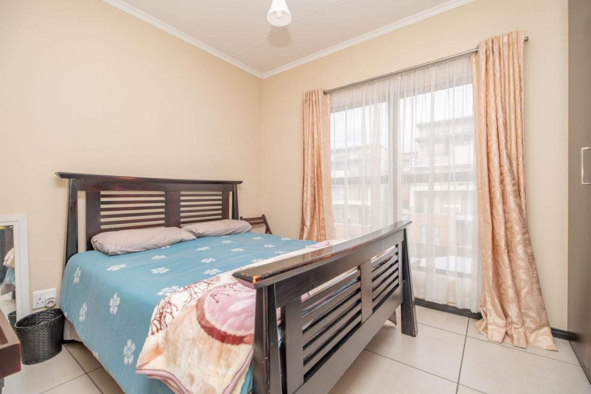 A bedroom featuring tiled flooring, neutral wall finishes, and a large window with curtain tracks, providing natural light and access to the exterior.